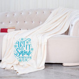 Let It Snow Somewhere Else Sublimation Transfer, image of a white blanket with a blue snowflake and text design on it draped over a beige tufted sofa.