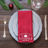 Product Christmas Tree Farm Tea Towel Screen Print Heat Transfer, red tea towel with Christmas tree farm design on a place setting with silverware, glass, and holiday decor.