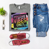 Positive Vibes Only Screen Print Heat Transfer, colorful and inspirational graphic on a gray t-shirt surrounded by denim jeans, red sneakers, a wristwatch, and a small potted plant.