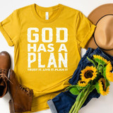 God Has A Plan Screen Print Heat Transfer, yellow t-shirt with white text, surrounded by a tan hat, sunflower bouquet, blue denim jeans, and brown shoes.