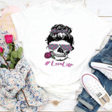 LoveLife Skeleton Sublimation Transfer, white t-shirt with a graphic of a skull wearing a pink and purple patterned blindfold and a pink rose in its mouth, surrounded by casual clothing and flowers.