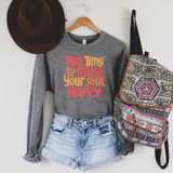 Take Time To Make Your Soul Happy Screen Print Heat Transfer, Grey sweatshirt with motivational quote in orange and red text, paired with denim shorts, brown hat on hook, and a patterned backpack hanging on the wall.
