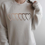 Unity Open Hearts ADULT Screen Print Heat Transfer, a beige sweatshirt featuring a row of five overlapping heart outlines in soft pink, peach, brown, and black, representing unity and love.