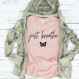 Just Breathe Screen Print Transfer, image showing a light pink T-shirt with 'just breathe' text and butterfly graphic, placed on a beige hoodie on a white wooden surface.