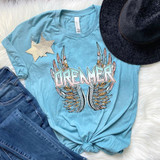 Dreamer Screen Print Heat Transfer, colorful graphic t-shirt with feather design, featuring the word DREAMER, laid on white faux fur with denim jeans and a black hat.