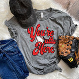 You're Outta Here Baseball Screen Print Heat Transfer, gray T-shirt with red lettering and baseball graphic, laid out with a black cap, blue jeans, and baseball gloves on a white furry surface.