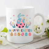 Happy Easter Sublimation Transfer, a white ceramic mug with colorful Easter-themed design featuring a bunny emerging from an Easter egg, surrounded by flowers and decorated eggs.