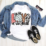 For The Love of The Game Volleyball Sublimation Transfer, a colorful t-shirt with a volleyball and leopard print design surrounded by casual accessories including a denim jacket, sunglasses, and Vans sneakers on a white wooden background.