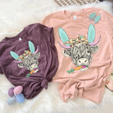Shaggy Cow Easter Screen Print Heat Transfer, illustrated cow wearing bunny ears, bow, and holding a carrot with Easter eggs on a soft fabric background.