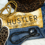 I'm A Hustler Don't Call Me Lucky Screen Print Heat Transfer, close-up of a yellow heat transfer sign with black text, surrounded by leopard print shoes, gold and black beaded necklaces, and denim jeans, emphasizing urban fashion style.