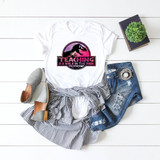 Teaching Is A Walk In The Park Sublimation Transfer, white T-shirt with dinosaur graphic and motivational text on a flat lay arrangement.