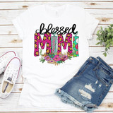 Blessed MIMI Sublimation Transfer T-shirt with colorful 'Blessed MIMI' design, floral and leopard print details, laid on a white wooden background with sneakers and ripped denim shorts.