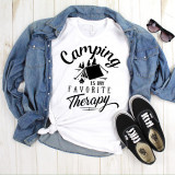 Camping Is My Favorite Therapy One Color Sublimation Transfer T-shirt with camping tent and trees graphic, paired with denim jacket, black Vans sneakers, and sunglasses, laid out on a wooden surface.