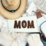 Dog Mom Brown & White Felt Chenille Embroidered Patch, embroidered patch with the word 'MOM' in brown felt and white outline, featuring paw print accents, on a white fabric background surrounded by accessories.