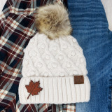 Falling Leaf Leather Patch, a brown leather patch with a falling leaf design sewn onto a white knit beanie.
