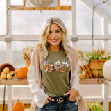 Nightmare Lattes DTF Heat Transfer, woman wearing a t-shirt with pumpkin spice latte designs in a cozy pumpkin-themed setting.