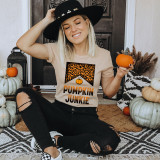 Pumpkin Junkie Screen Print Heat Transfer, a woman wearing a beige t-shirt with Halloween pumpkin and leopard print design, sitting with pumpkins around her, holding a small pumpkin, in a festive autumn setting.