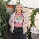Yuletides & Hippie Vibes Screen Print Heat Transfer, a woman wearing a pink t-shirt with a colorful design featuring a retro van, a rainbow, and trees, celebrating holiday and boho styles.