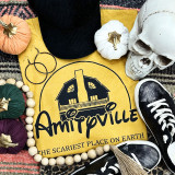 Amityville Screen Print Heat Transfer, yellow fabric with the Amityville haunted house logo and text, surrounded by pumpkins, skull, sneakers, earrings, and wooden beads.
