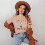 These Boo's Were Made For Spookin' Screen Print Heat Transfer, a woman wearing a pastel pink t-shirt with a spooky ghost illustration and humorous text, complemented by a brown hat and jacket.