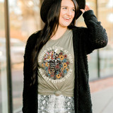 Would Ya Look At That Screen Print Heat Transfer, a woman wearing a gray T-shirt with a skeleton and floral design, and humorous text, standing outdoors with a black cardigan and a black hat.
