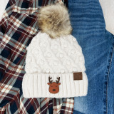 Reindeer Leather Patch, a decorative leather patch featuring the letter 'C.C.' on a cozy white knit winter hat with a reindeer graphic, placed on a person's lap surrounded by a plaid shirt and blue jeans.