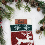 Custom Text Brown Leather Patch, a personalized leather patch attached to a Christmas sock with snowflakes and reindeer design, surrounded by holiday greenery and pinecones.
