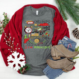 I'm Booked DTF Transfer, Christmas-themed gray T-shirt with colorful travel and holiday icons, displayed with red sweater, jeans, and boots on a festive background.