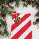 Custom Initial Brown Leather Patch, Christmas-themed product with a red and white striped knit fabric and a brown leather patch engraved with 'S' for personalization, surrounded by pine branches and pinecones for holiday decoration.