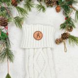 Custom Initial TAN Leather Patch, cream knitted winter scarf with a monogrammed leather patch featuring the letter 'K' on a white fluffy surface surrounded by pine branches and pine cones for Christmas decoration.