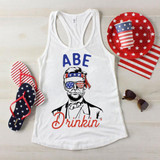 Abe Drinkin' Patriotic Sublimation Transfer, a tank top with a patriotic design featuring Abraham Lincoln wearing American flag-themed sunglasses and a headband, surrounded by red, white, and blue accessories with stars and stripes.