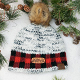 Not Made For Winter TAN Leather Patch, knit winter beanie with a fur pom-pom and a leather patch displayed among pine branches and pinecones.