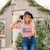 Jingle Bell Rockin' Screen Print Transfer, woman wearing a pink t-shirt with Christmas tree graphic and text, outdoors in front of a decorated holiday house.