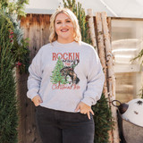 Rockin Around The Christmas Tree DTF Heat Transfer, Christmas-themed sweatshirt with a graphic of a reindeer riding a horse next to a decorated Christmas tree.