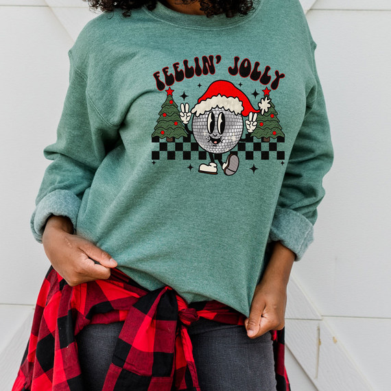 Feelin' Jolly DTF Heat Transfer, Christmas-themed graphic sweatshirt featuring a cheerful emoji wearing a Santa hat, surrounded by Christmas trees and holiday decorations.