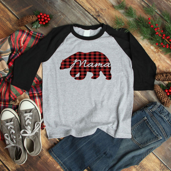 Mama Bear Buffalo Plaid DTF Heat Transfer, a red and black buffalo plaid bear silhouette design on a gray and black raglan t-shirt, surrounded by festive holiday decorations and casual clothing items.