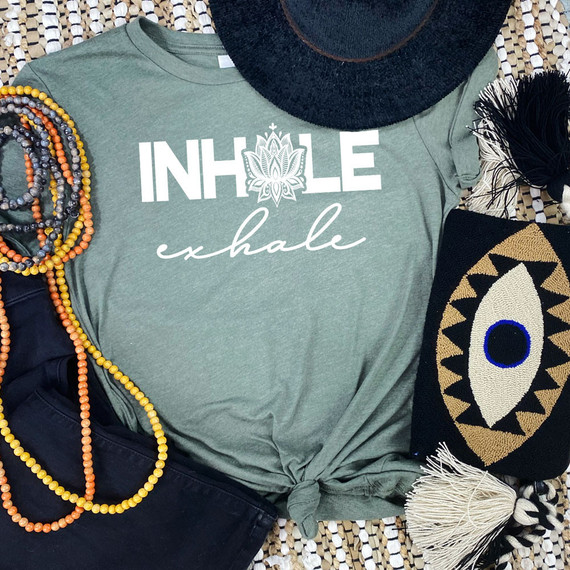 Inhale Exhale Lotus WHITE DTF Heat Transfer, white design with lotus flower and text on a green T-shirt, surrounded by colorful beads, black hat, and decorative items.