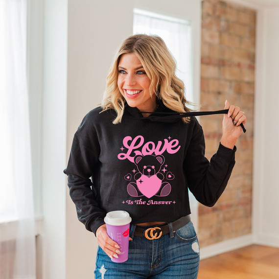 Love Is The Answer DTF Heat Transfer, close-up of a young woman holding a coffee cup and wearing a black hoodie with pink love bear design and text.