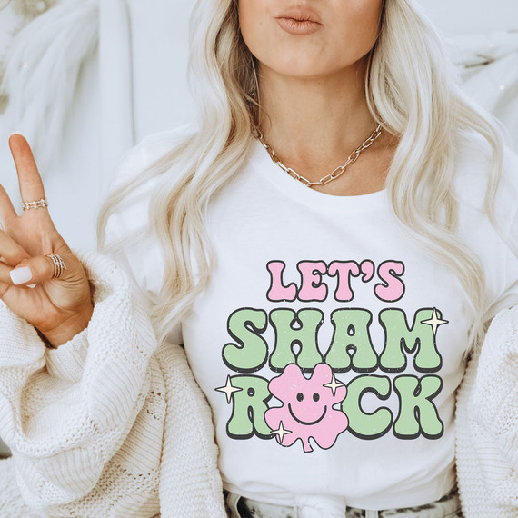 Let's Shamrock DTF Heat Transfer, printed on a white t-shirt featuring a pink shamrock with a smiley face and the text 'Let's Shamrock' in pink and green with star accents.