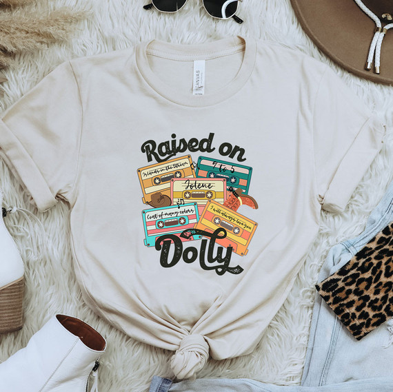 Raised On Dolly Cassette Tapes DTF Heat Transfer, colorful cassette tape design on a cream-colored T-shirt.