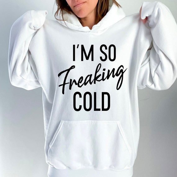 I'm So Freaking Cold DTF Heat Transfer, women wearing a white hoodie with bold and script black text saying 'I'M SO Freaking COLD'. 
