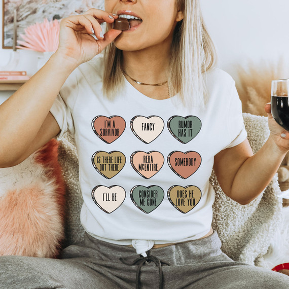 Reba Candy Hearts DTF Heat Transfer, colorful heart-shaped stickers with words and phrases, worn on a woman's white t-shirt in a casual setting.