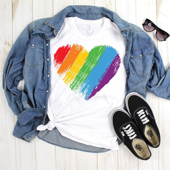 Brush Stroke Watercolor Rainbow Heart Pride Sublimation Transfer, colorful watercolor heart design in rainbow colors on a white T-shirt, draped with a denim jacket, sunglasses, and sneakers in the image.