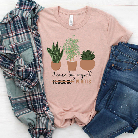 I Can Buy Myself Plants DTF Heat Transfer, pink T-shirt with a graphic of three potted plants and the text 'I can buy myself flowers plants' printed on it, laid flat alongside a plaid shirt and denim jeans on a white background.