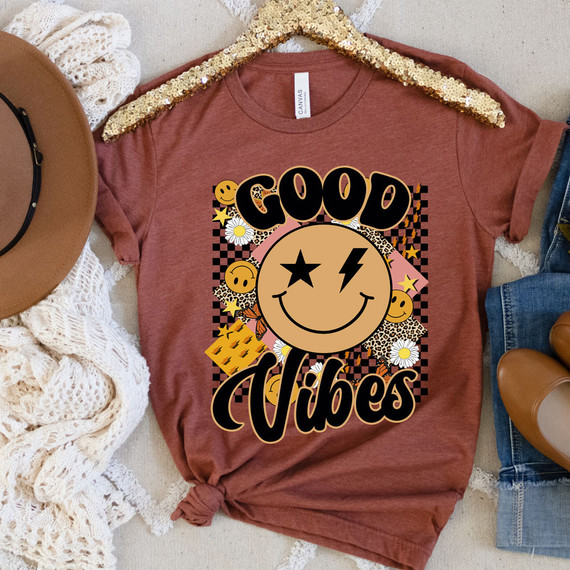 Good Vibes Happy Face DTF Heat Transfer, colorful smiley face graphic with stars, hearts, and floral elements on a casual t-shirt.