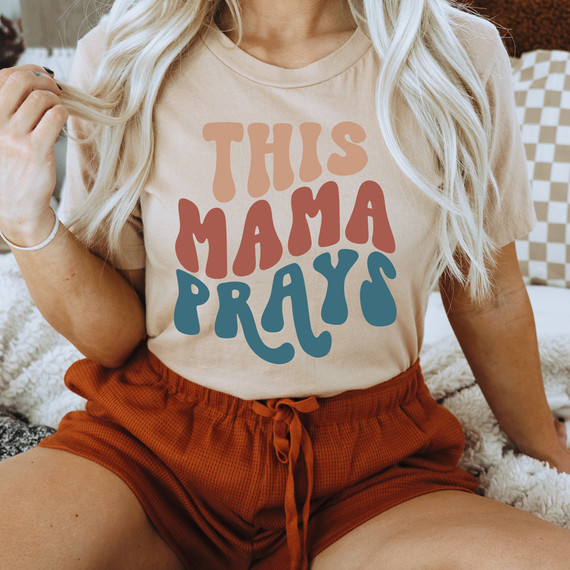 This Mama Prays DTF Heat Transfer, beige t-shirt with colorful text design.