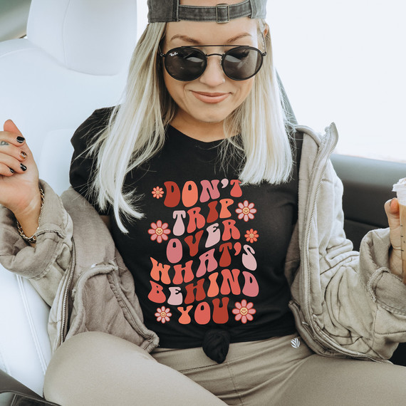 Don't Trip Over What's Behind You DTF Heat Transfer, close-up of a woman wearing a black T-shirt with the phrase and floral design, sitting in a vehicle.