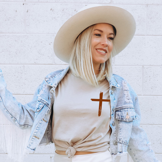 Distressed Cross DTF Heat Transfer, a brown cross design on a woman's beige t-shirt.