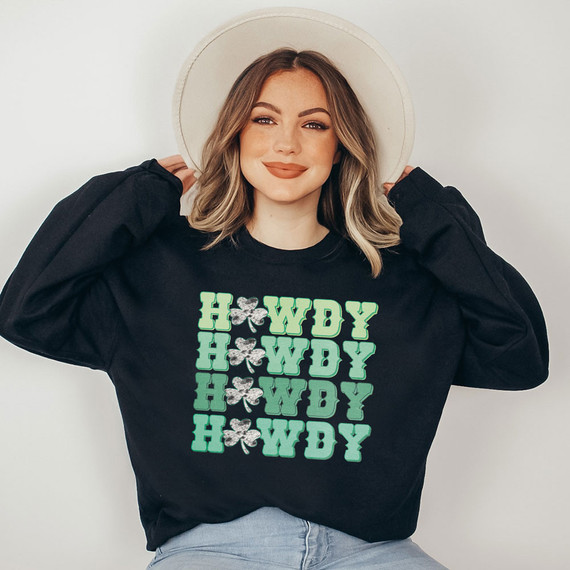 Howdy Stacked DTF Heat Transfer, a woman showcasing a black sweatshirt with a stacked 'Howdy' design featuring shamrock accents.
