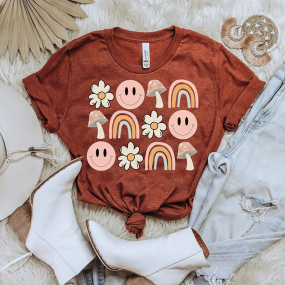Boho Flowers & Rainbows Screen Print Heat Transfer, colorful boho flowers, rainbows, smiling faces, and mushrooms design on a rust-colored t-shirt.